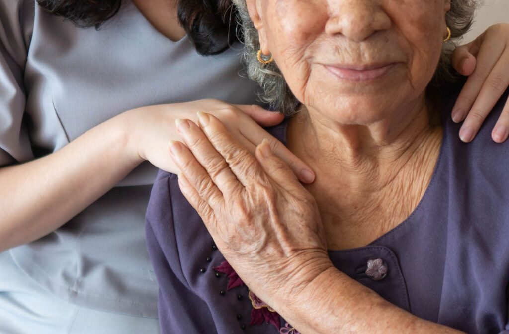 A caregiver supports an appreciative older adult while they both smile for a picture