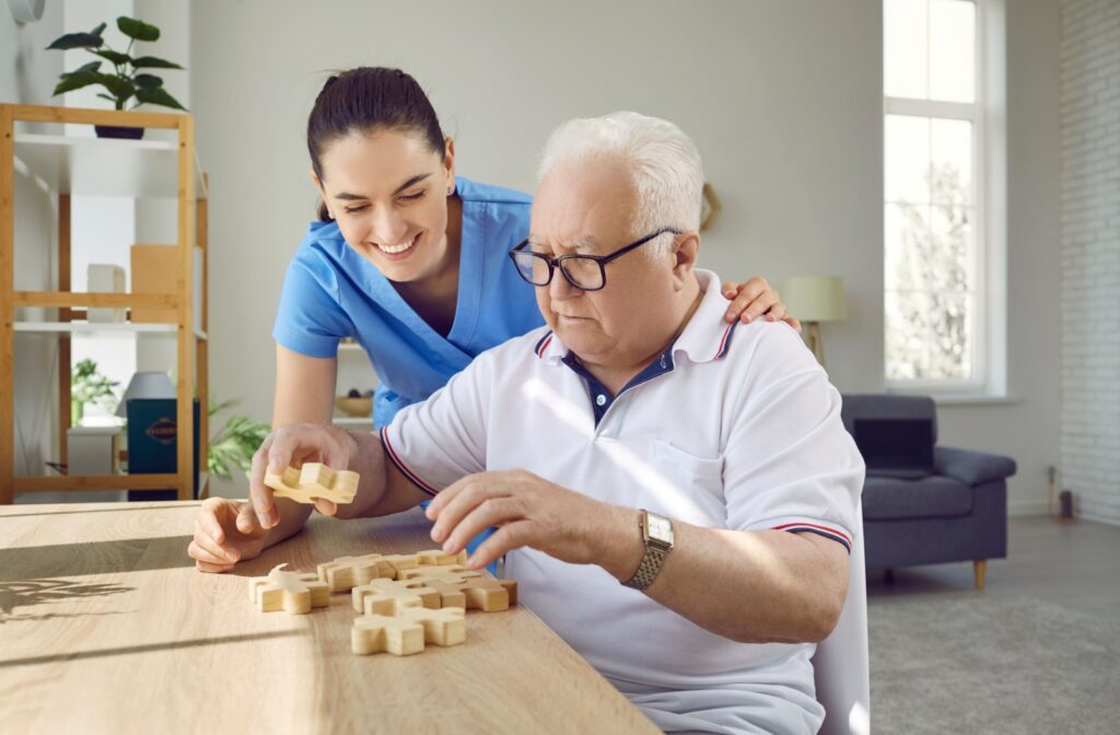 A caregiver laughs while handing an older adult a wooden puzzle block during activity time in memory care
