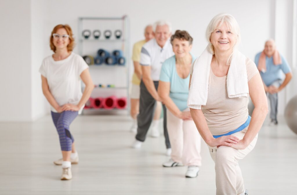 A group of older adults in senior living perform lunges to stretch their legs during a community fitness class