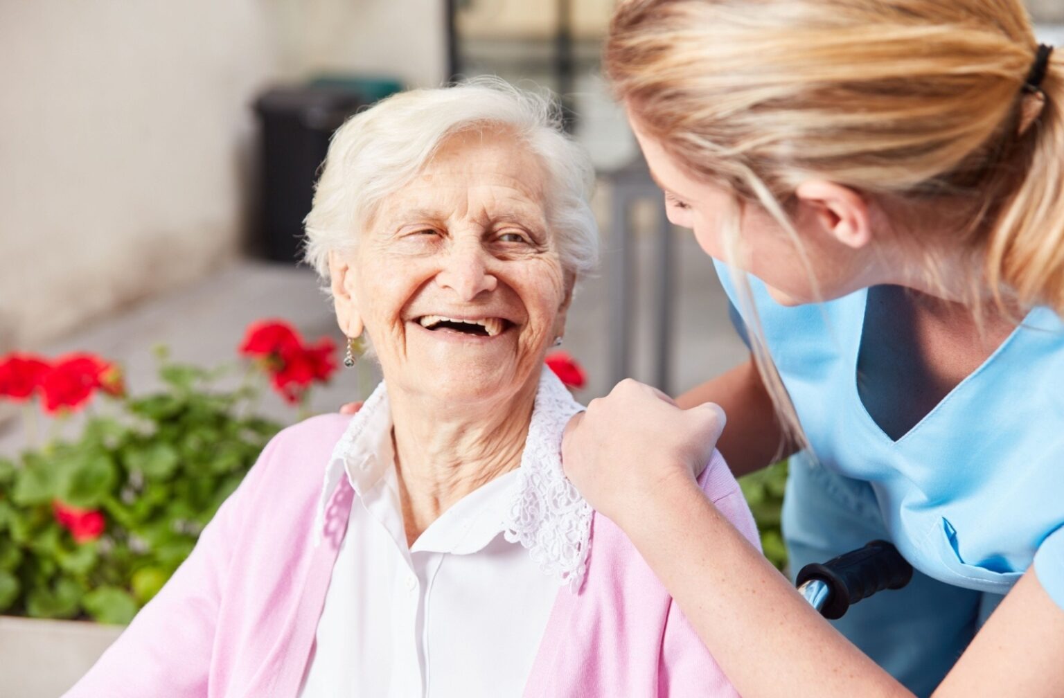 A senior smiles at a caregiver resting a hand on their shoulder